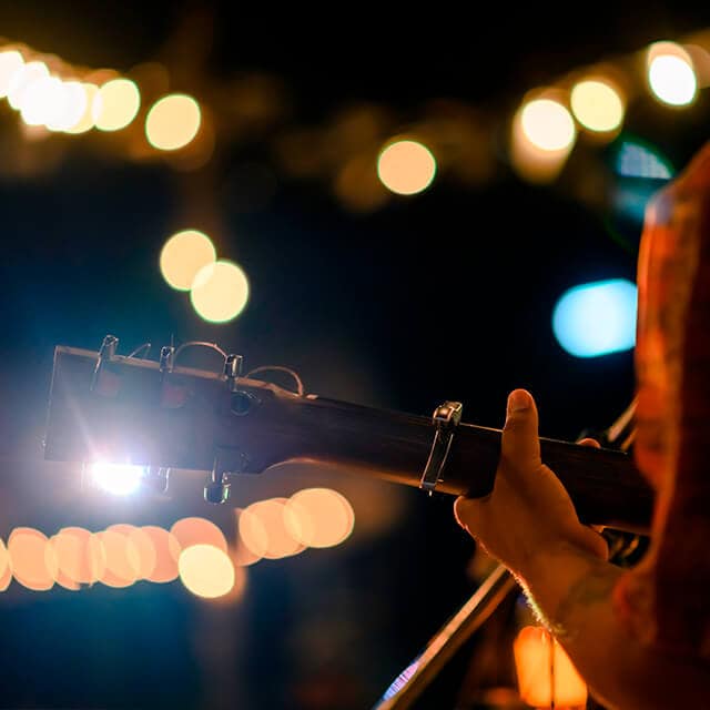 The headstock and neck of an acoustic guitar are backlit by stage lights during a performance.