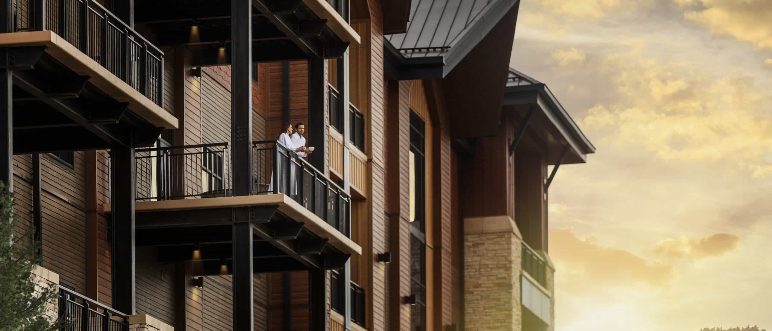 a man and woman stand on a balcony in white bathrobes during golden hour.