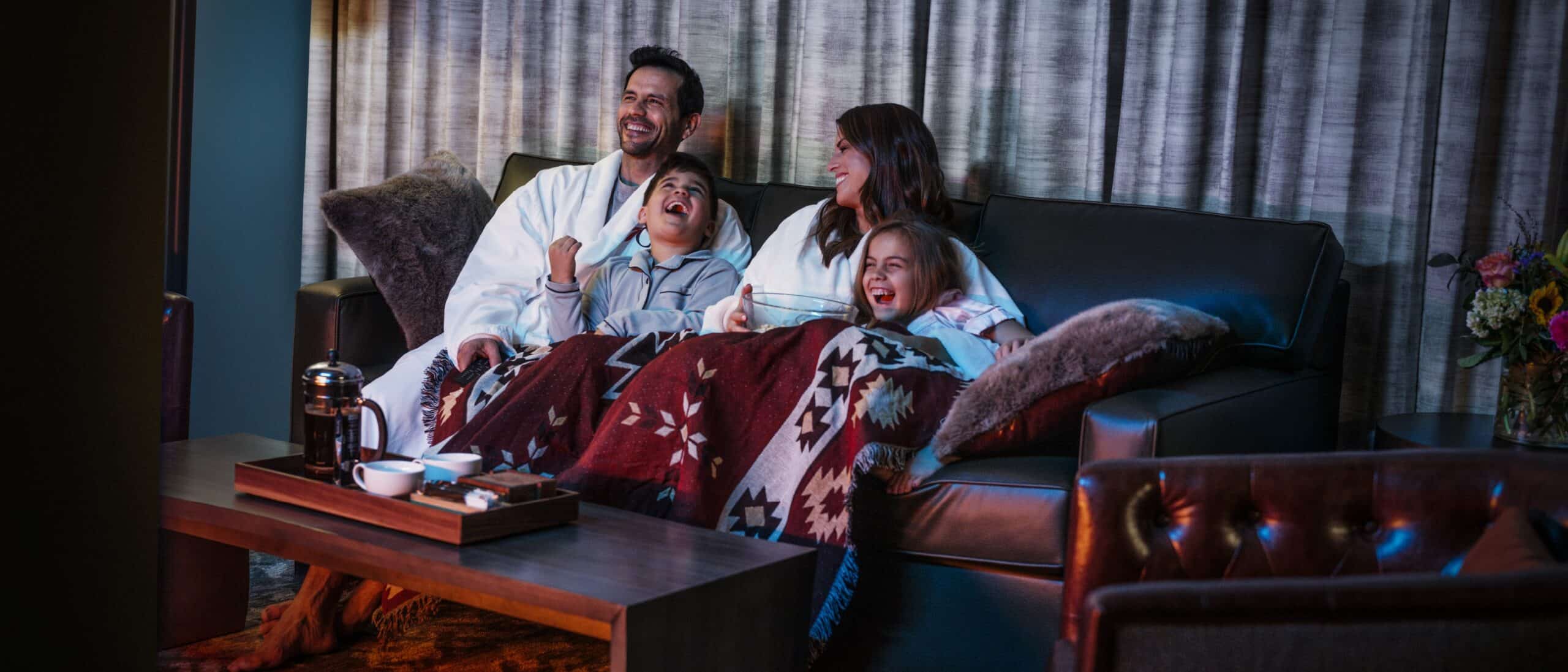 a family of four snuggle on a couch, laughing