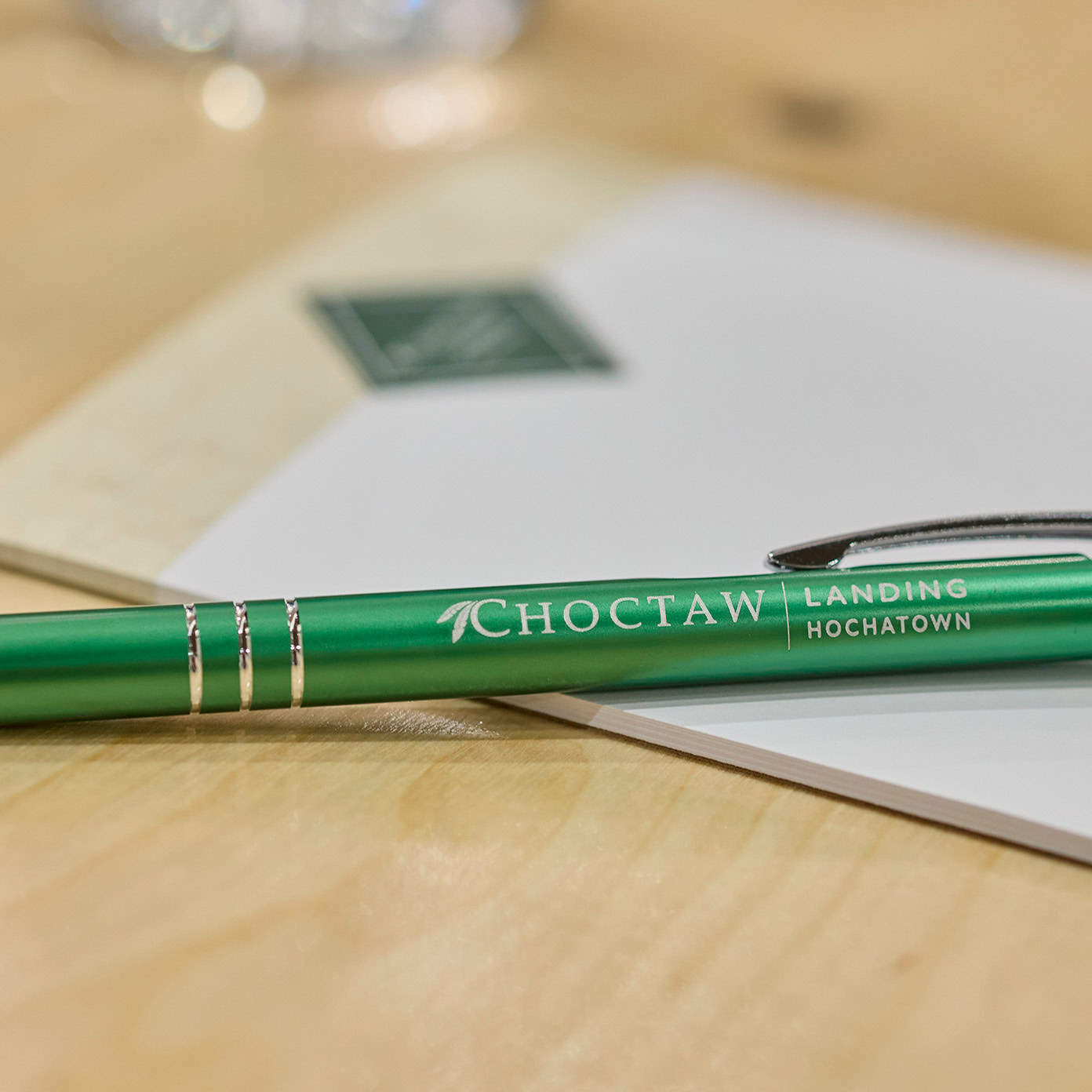 A green ballpoint pen with the "Choctaw Landing Hochatown" logo rests on a notepad on a wood table top.