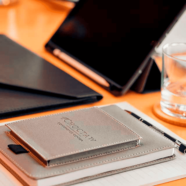 A notepad with the the words "Choctaw Conference Center" sits neatly stacked upon other writing materials on a desk. In the background is an iPad and a glass of water.