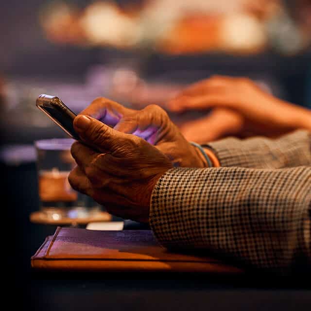 A pair of hands resting on a table holds a smart phone.