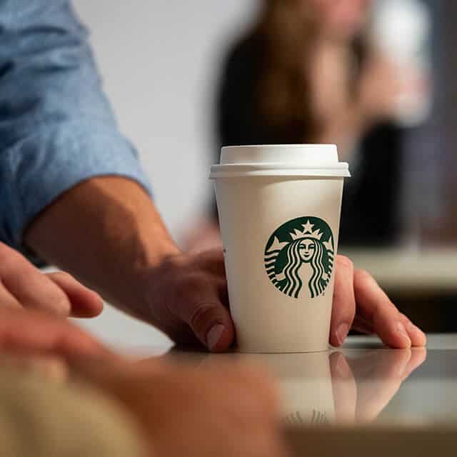A white Starbucks cup being held at the base sits on a surface.