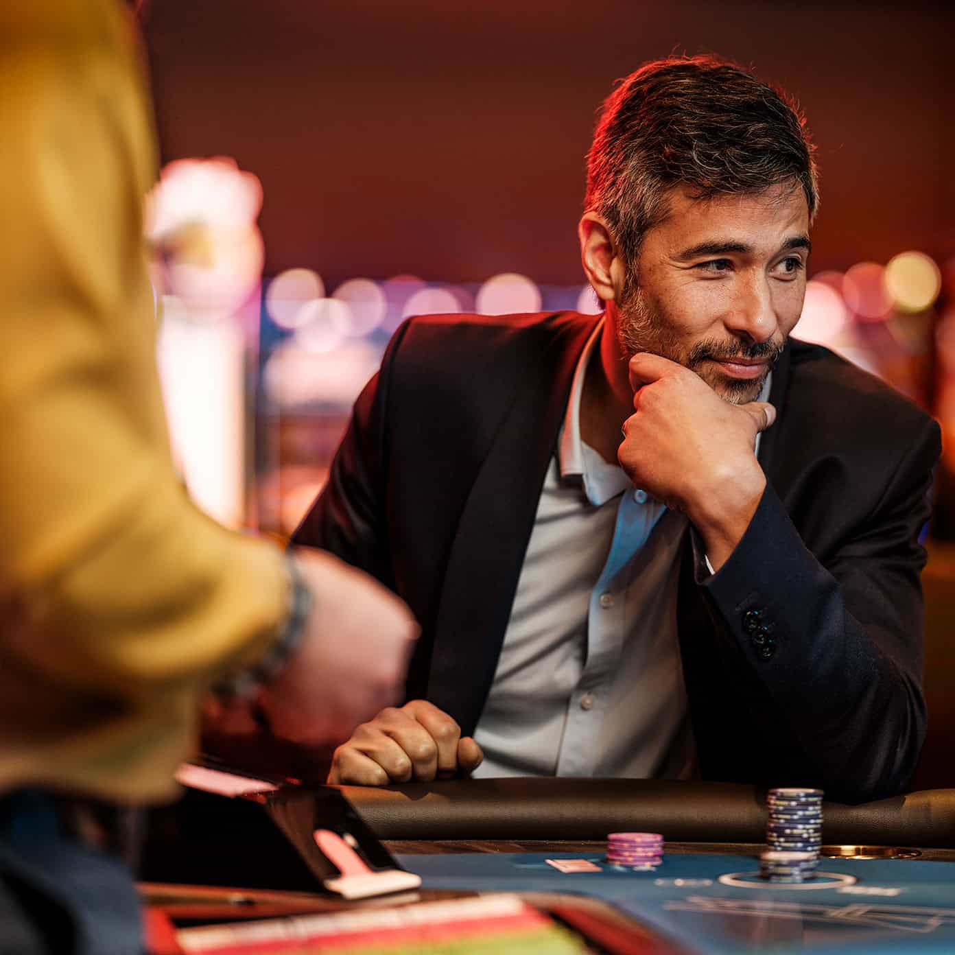 A man in a blazer sits pensively at a blackjack table.