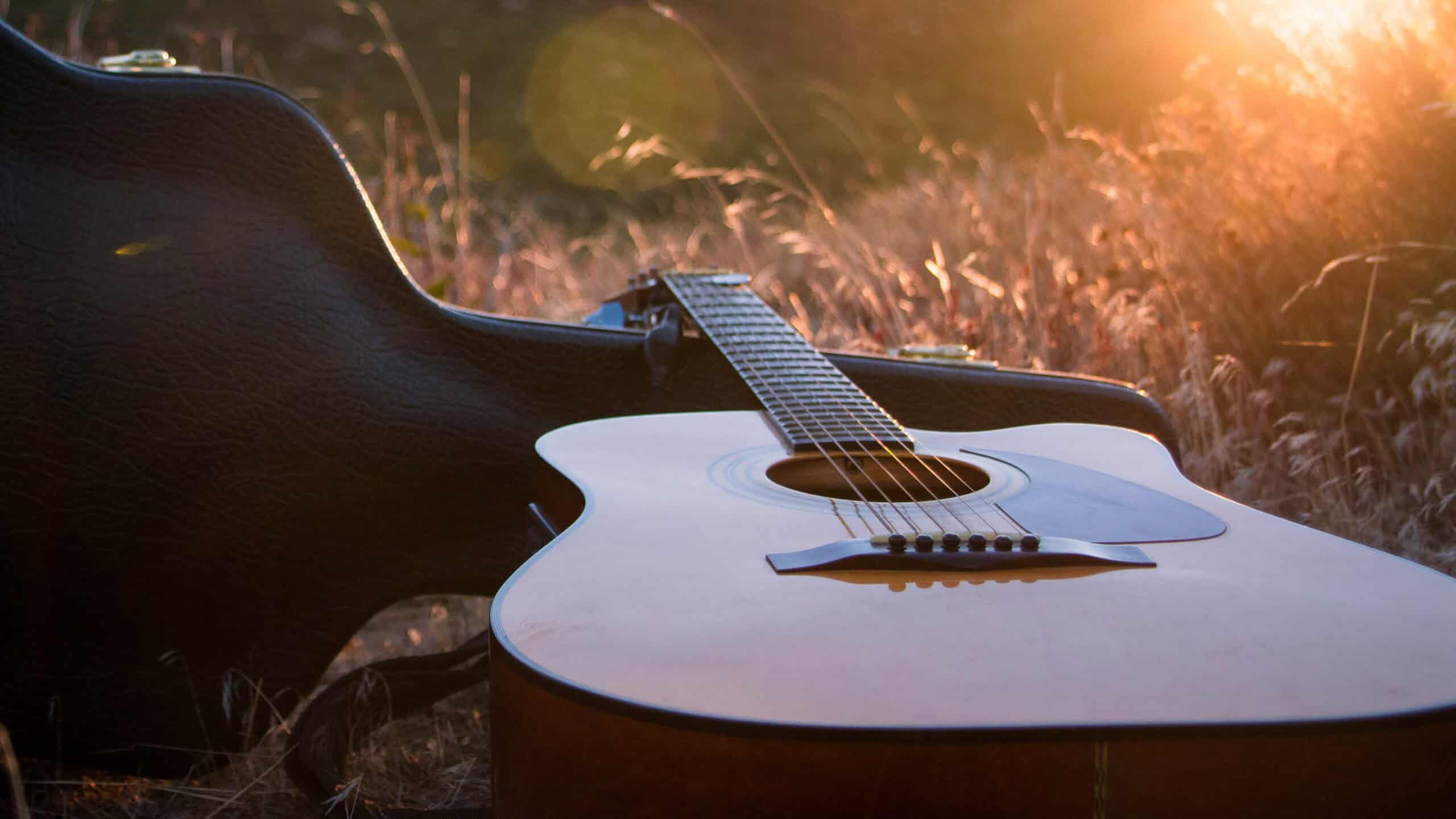 an acoustic guitar lays against an open guitar case in a meadow during golden hour