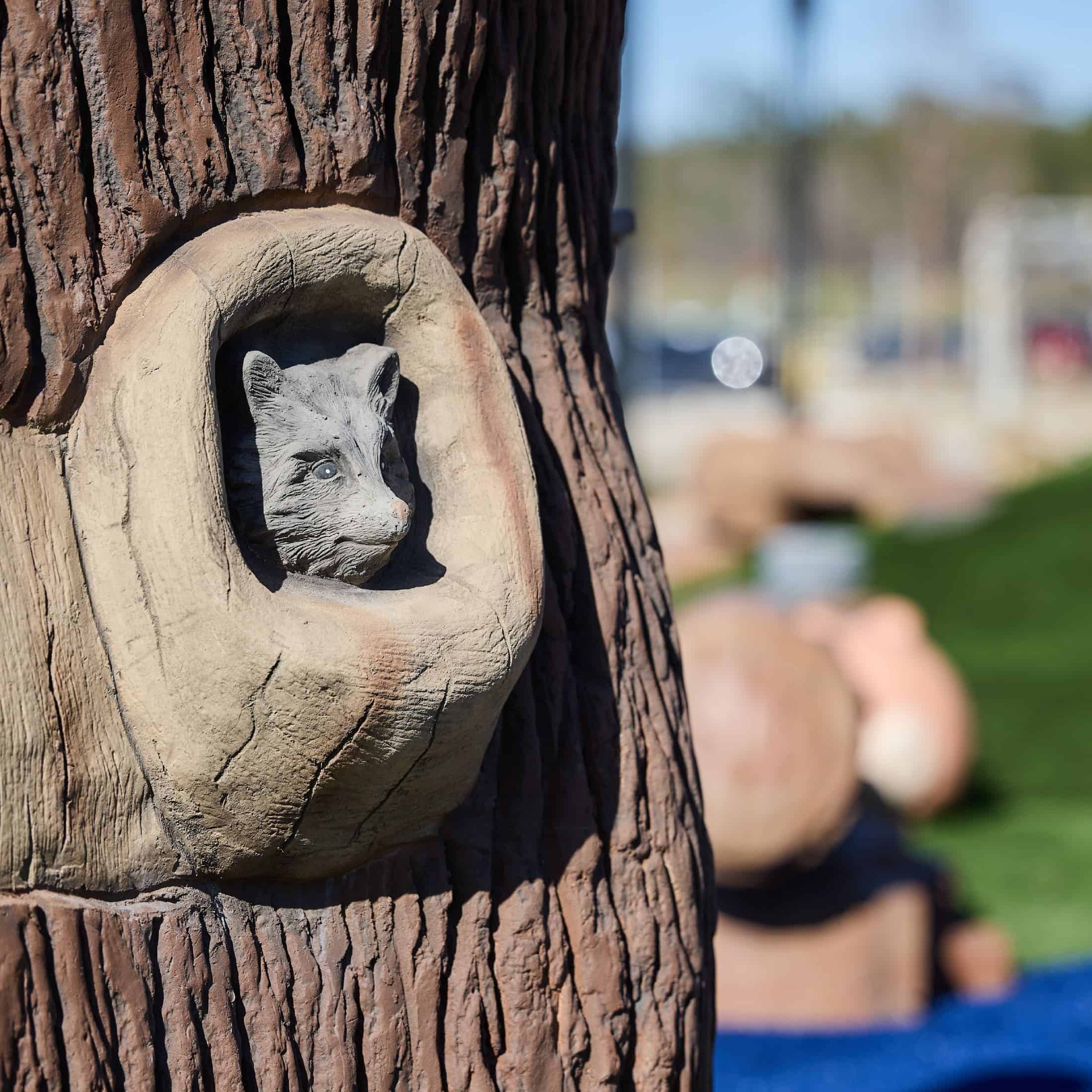 A sculpted animal peeks out of a fake tree hole