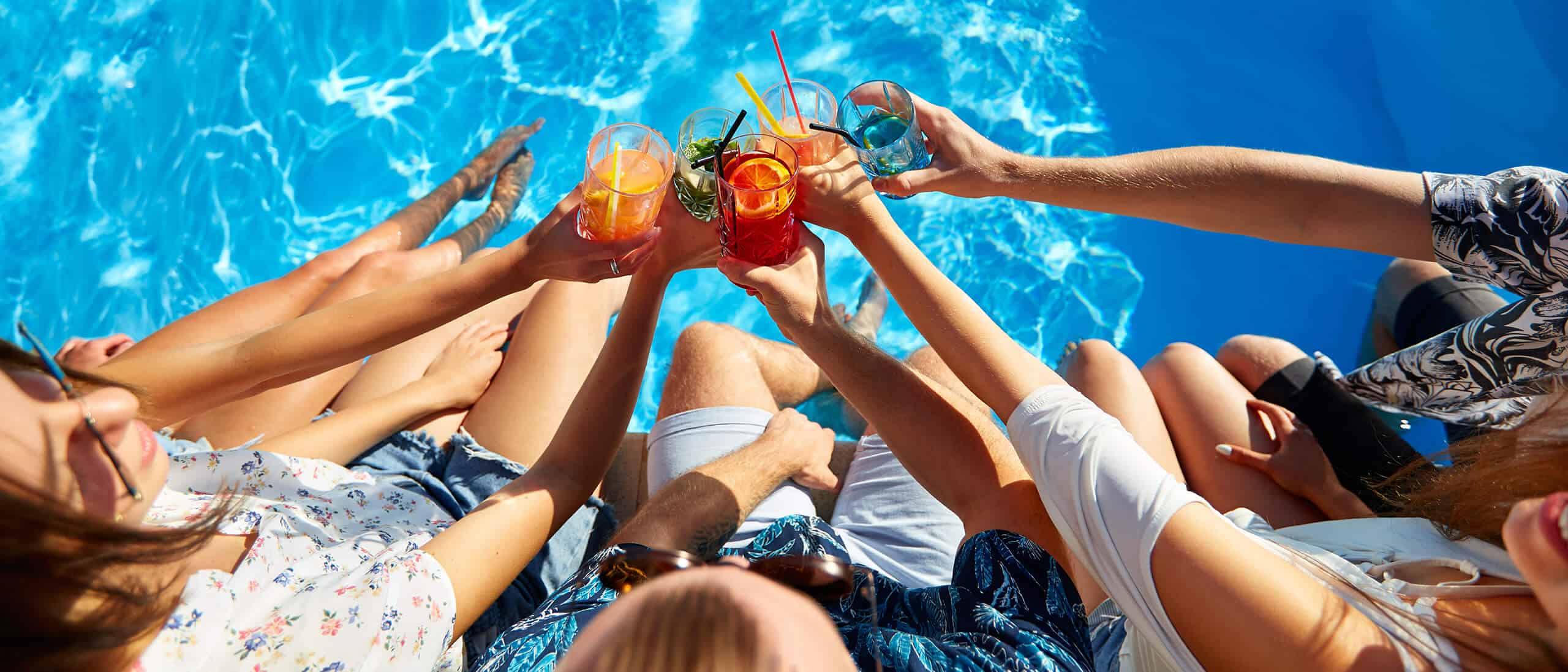 People toasting drinks over a blue pool.