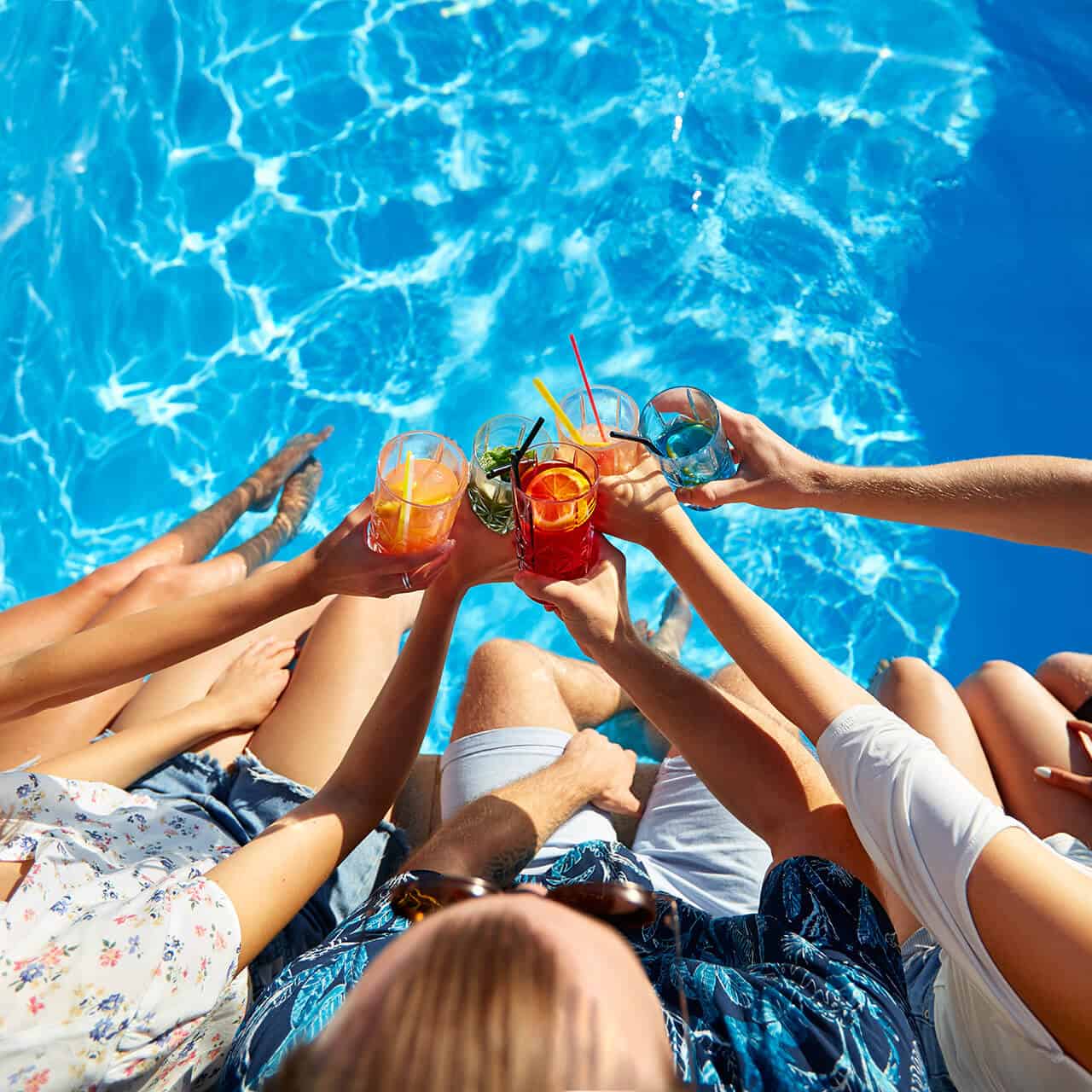 People toasting drinks over a blue pool.